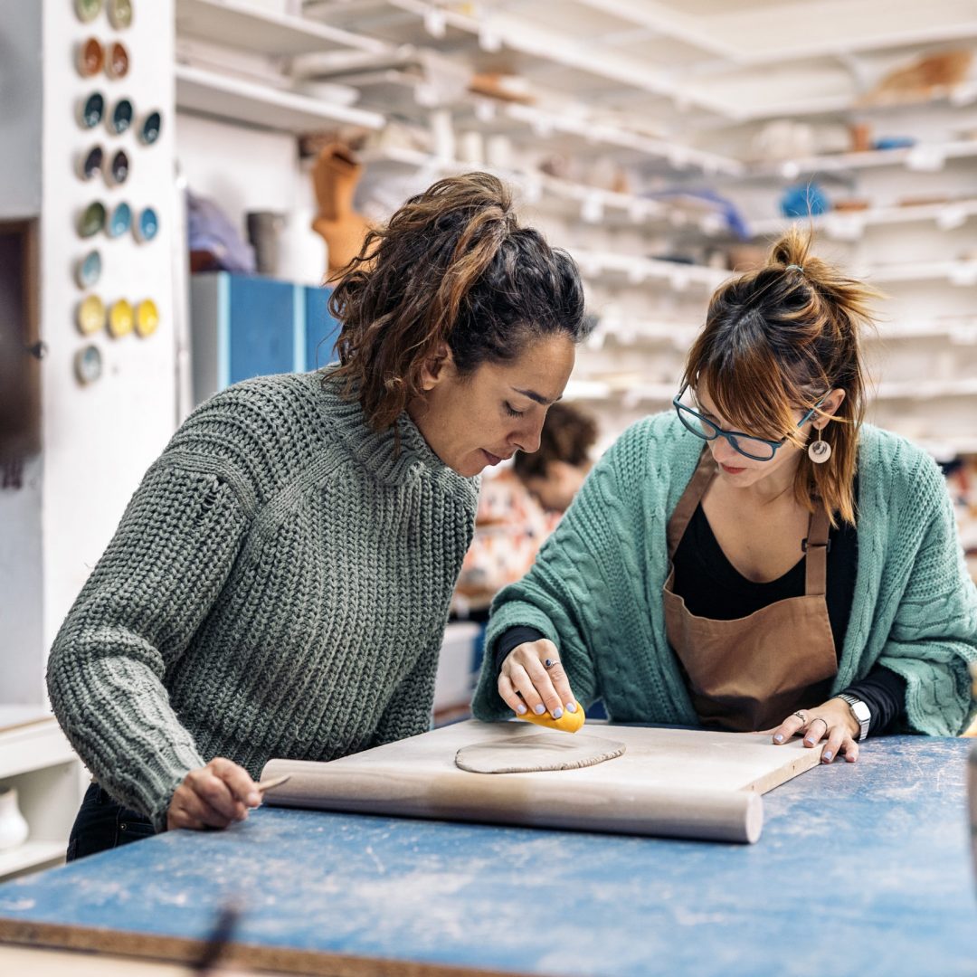 Stock photo of potter teacher in apron working in pottery atelier and using clay.
