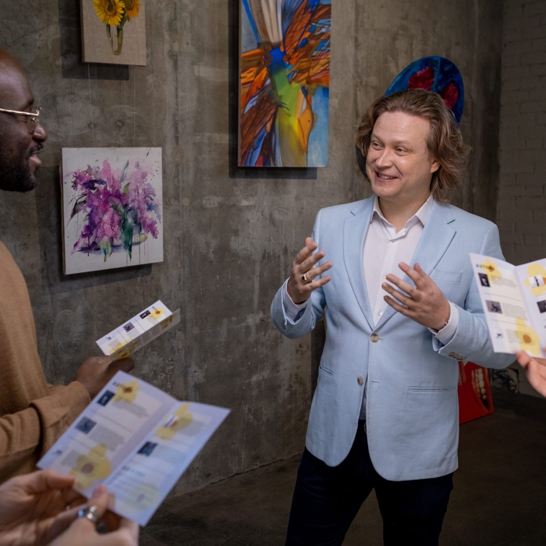 Happy elegant artist interacting with intercultural guests of exhibition of his artworks in gallery